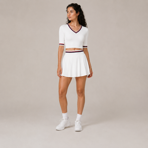 Model wearing the Fitfigura Ace Set – Signature Court Form in white, featuring a V-neck top with contrast trim and a matching pleated skirt, shown from the front.