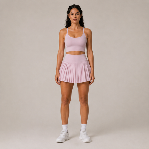 Model wearing the Fitfigura Ace Skirt – Pleated Form in light pink with a matching crop top, white socks, and white sneakers, shown from the front.
