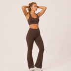 Model posing in the brown Fitfigura Balance Flare Pant – Sculpt Silhouette with arms raised, highlighting the flared leg and fitted waist.