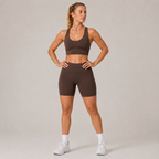Model wearing the Fitfigura Contour Bra – Defined Sculpt in dark brown with matching shorts, shown from the front with a supportive scoop neckline.