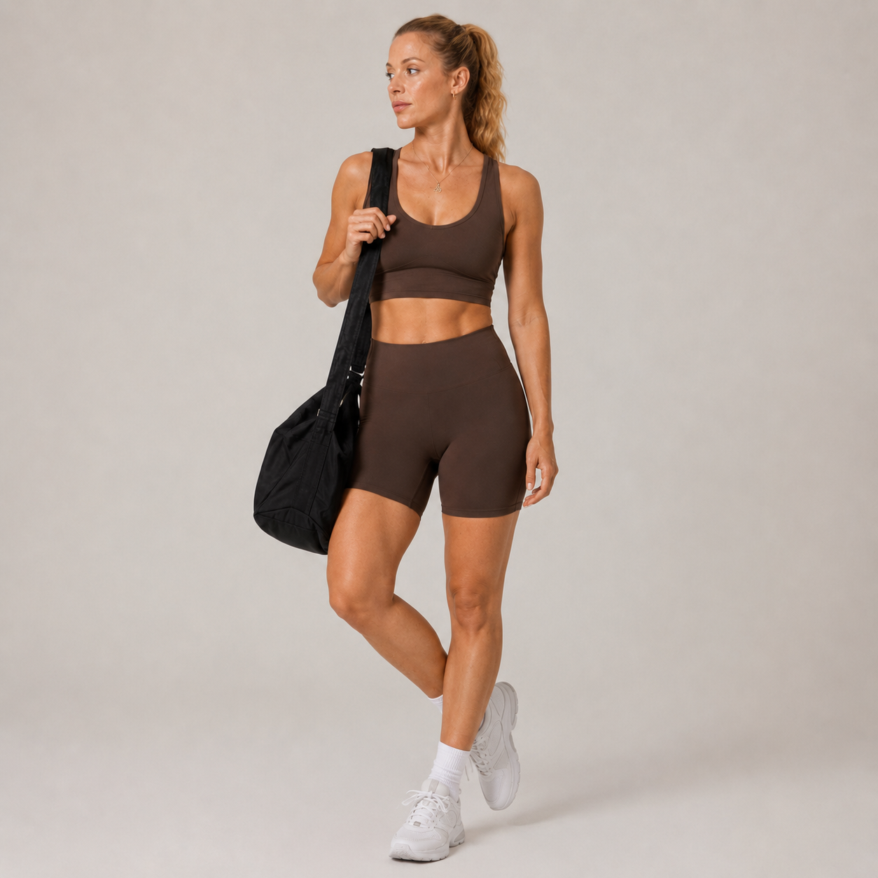 Model wearing the Fitfigura Contour Bra – Defined Sculpt in dark brown with matching shorts and a black gym bag.