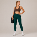 Model wearing the Fitfigura Core Compression Legging in deep teal with a brown sports bra, white socks, and a black gym bag, shown from the front.