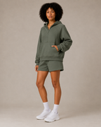 Model posing in the olive green Fitfigura Core Hoodie – Essential Form, highlighting the oversized hoodie and matching short set.