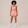 Model wearing the Fitfigura Core Set – Minimal Sculpt Form in coral pink, featuring a sleeveless crop top and matching skirt, shown from the front.