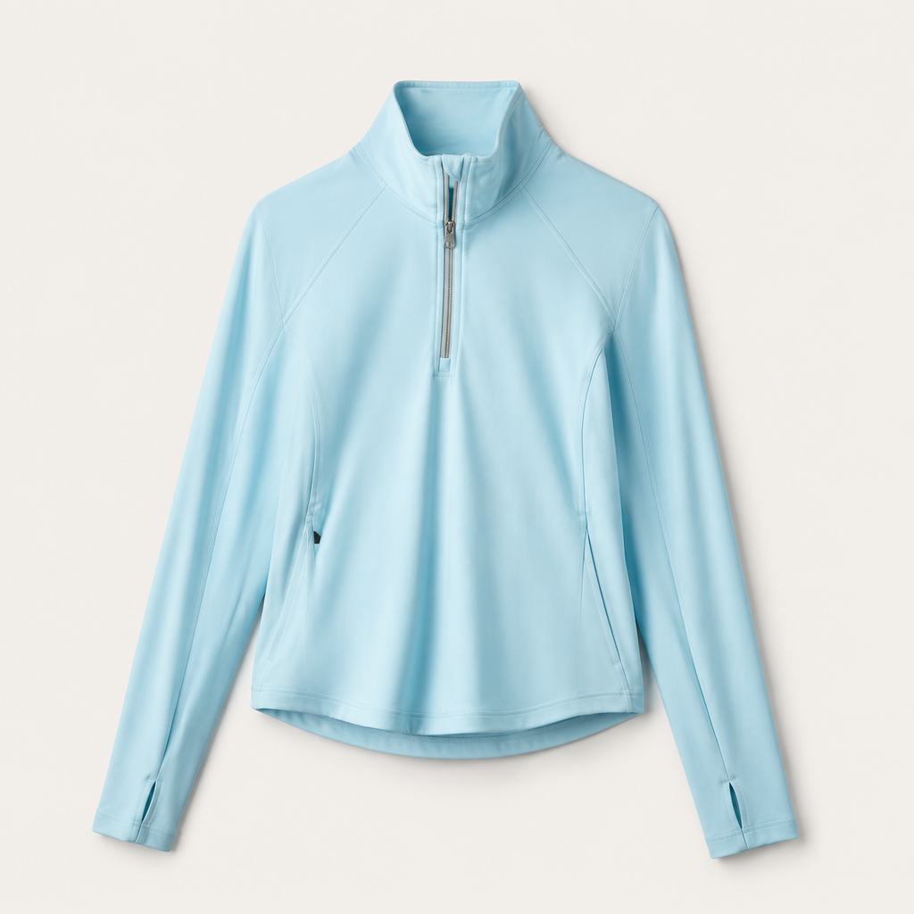 Flat lay of the Fitfigura Course to Court 1/4 Zip Top in light blue, showing the quarter-zip collar, long sleeves, and curved hem.