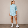 Model wearing the Fitfigura Course to Court 1/4 Zip Top in light blue with a matching skirt, white socks, and white boots, shown from the front.