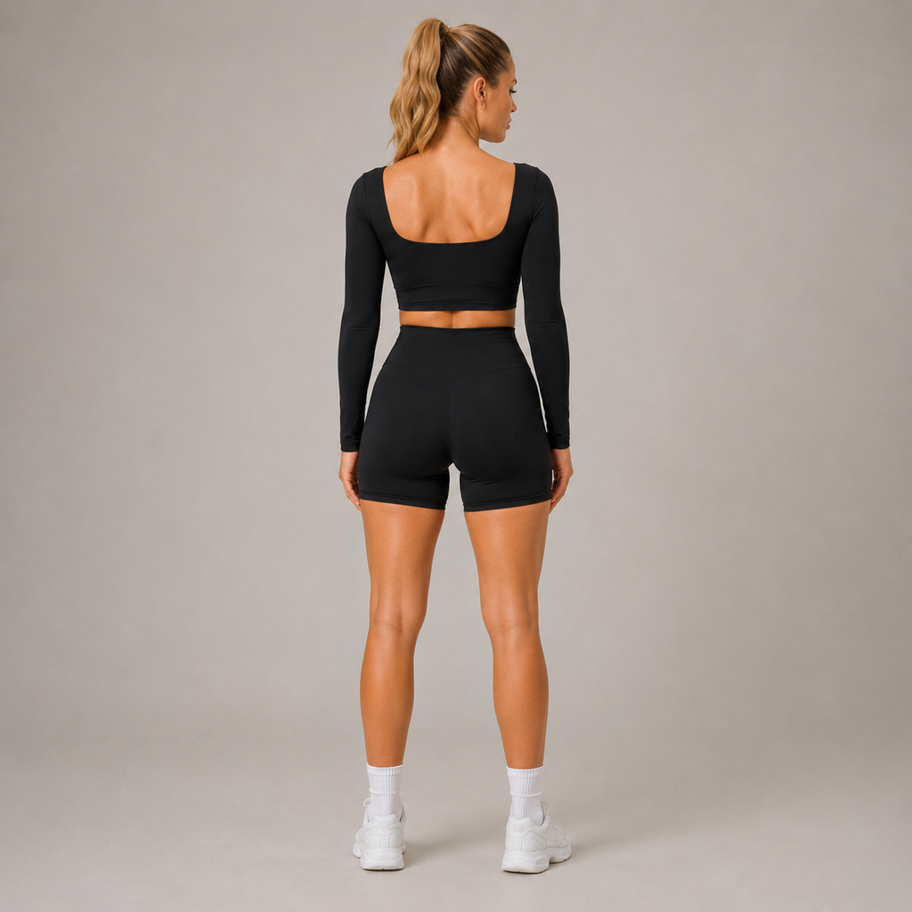Back view of the black Fitfigura Freedom Scoop Long Sleeve Crop Top styled with matching shorts and white sneakers.