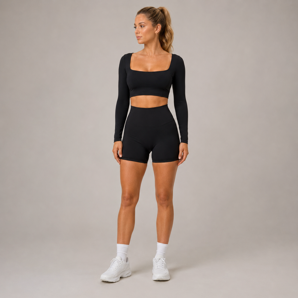 Full-body studio view of the black Fitfigura Freedom Scoop Long Sleeve Crop Top styled with matching shorts and white sneakers.