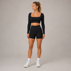 Full-body studio view of the black Fitfigura Freedom Scoop Long Sleeve Crop Top styled with matching shorts and white sneakers.