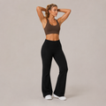 Model wearing the Fitfigura Lounge Flare Pant – Relaxed Luxury Form in black with a brown sports bra, shown from the front with a high-waist fit and flared legs.