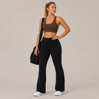 Model wearing the black Fitfigura Lounge Flare Pant – Relaxed Luxury Form with a brown sports bra and carrying a black bag.