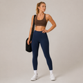 Model wearing the Fitfigura Pocket Legging in navy blue with a brown sports bra, white socks, and a black gym bag, shown from the front.