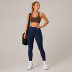 Model wearing the Fitfigura Pocket Legging in navy blue with a brown sports bra, white socks, and a black gym bag, shown from the front.
