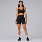 Model wearing the Fitfigura Pocket Short – Utility Performance Form in black with a matching black sports bra and black sneakers, shown from the front.