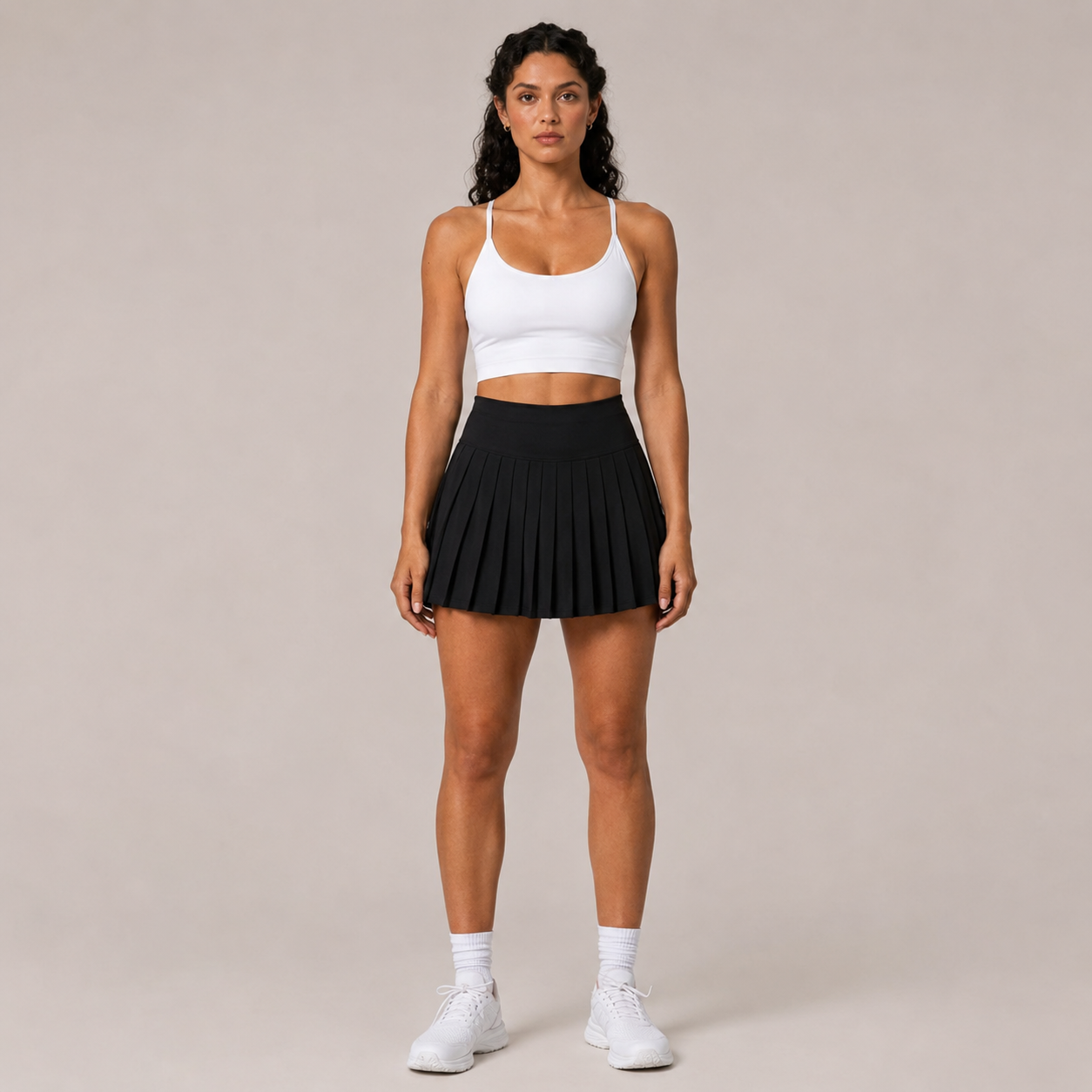 Model wearing the Fitfigura Rally Tennis Skirt – Sculpt Court Form in black with a white crop top, white socks, and white sneakers, shown from the front.