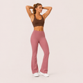 Model wearing the Fitfigura Rib Knit Flare Pant – Textured Luxe Form in dusty pink with a brown sports bra, shown from the front with a high-waist fit and flared legs.