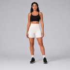 Model wearing the Fitfigura Rib Short – Soft Sculpt Form in white with a black sports bra and black sneakers, shown from the front.