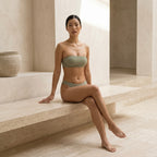 Model seated on a stone ledge in the sage green Fitfigura Sculpt Bikini – Contour Form, highlighting the smooth contour fit and minimal silhouette.