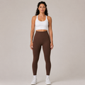 Model wearing the Fitfigura Sculpt Legging in dark brown with a white crop top and white socks, shown from the front.