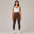 Model wearing the Fitfigura Sculpt Legging in dark brown with a white crop top and white socks, shown from the front.