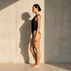 Side-angle view of the black Fitfigura Sculpt One-Piece SwimWear – Contour Form with natural shadow detail, emphasizing the sculpted body-contour design.