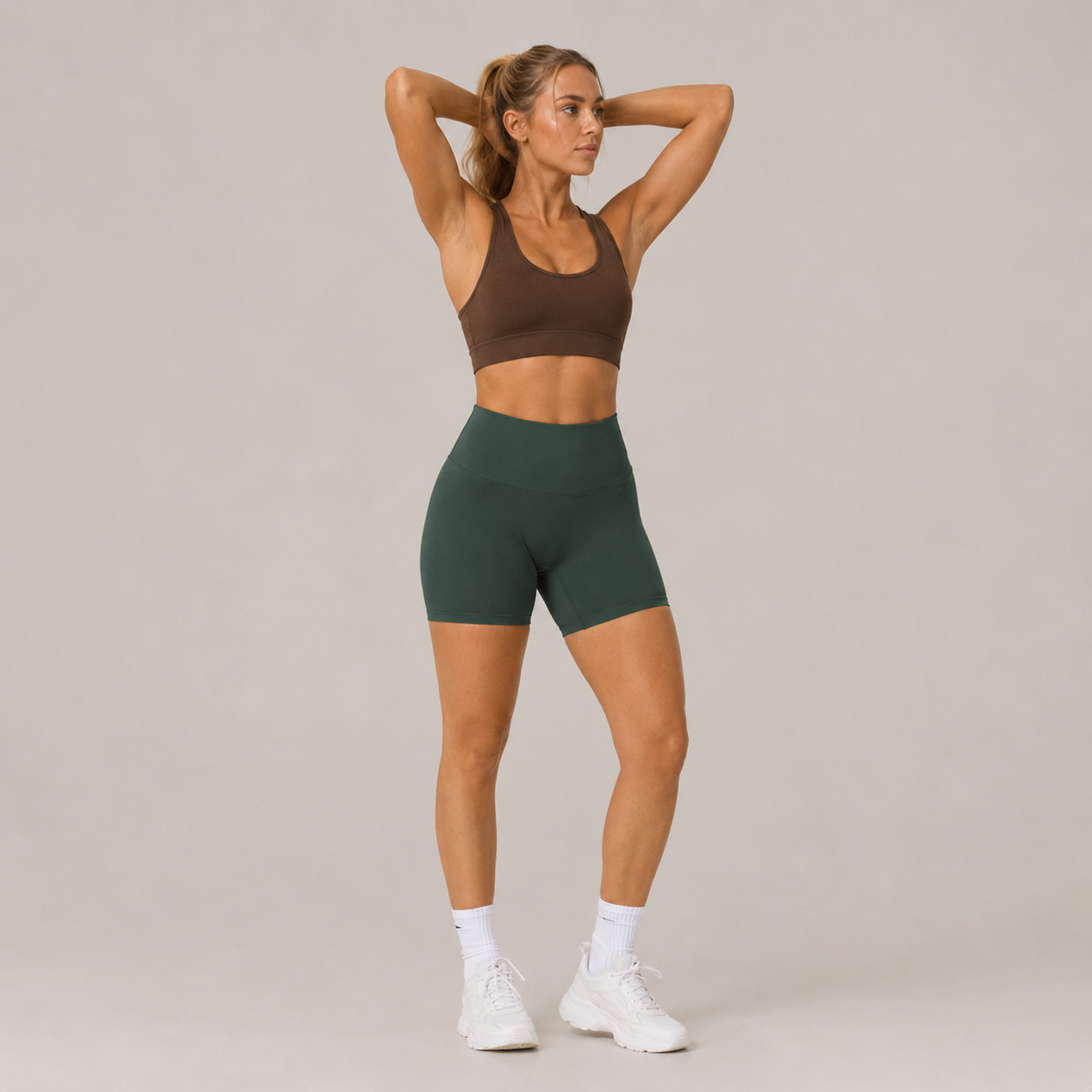 Model wearing the Fitfigura Seamless Short – Athletic Form in dark green with a brown sports bra, white socks, and white sneakers, shown from the front.
