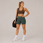 Model wearing the dark green Fitfigura Seamless Short – Athletic Form with a brown sports bra and carrying a black bag.