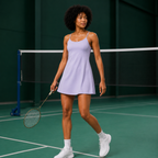 Model wearing the light purple Fitfigura Serve Dress – Elite Court Form on a tennis court, holding a racket in a ready stance.