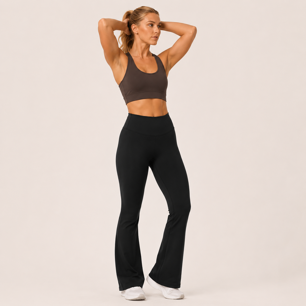 Model wearing the Fitfigura Studio High Waist Flare Pant – Fluid Motion Form in black with a matching black sports bra, shown in a front-facing pose with flared legs and a high-rise fit.