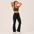 Model wearing the Fitfigura Studio High Waist Flare Pant – Fluid Motion Form in black with a matching black sports bra, shown in a front-facing pose with flared legs and a high-rise fit.