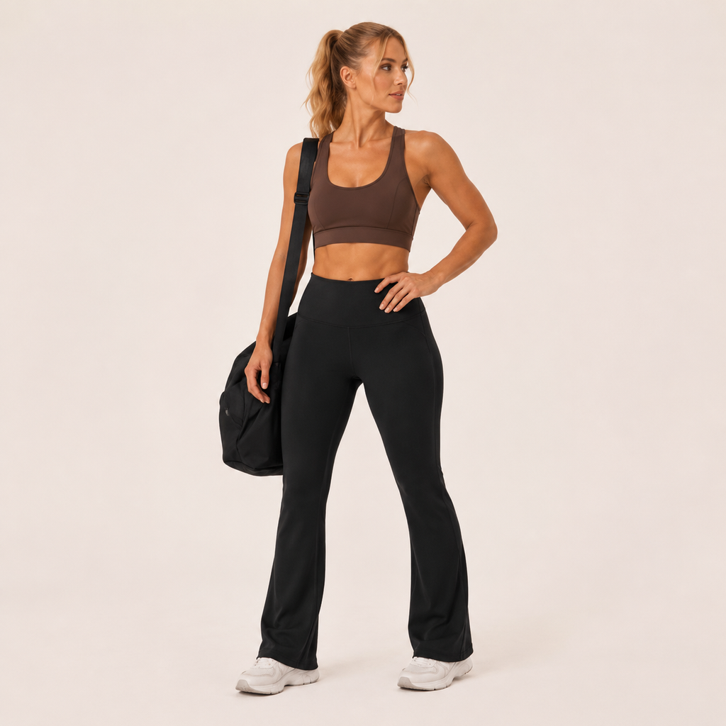 Model wearing the black Fitfigura Studio High Waist Flare Pant – Fluid Motion Form with a matching top and carrying a black bag.