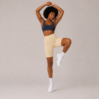 Model wearing the cream Fitfigura Studio Short 8” – Flow Essential Form in a leg-lift pose, highlighting the flexible activewear fit.