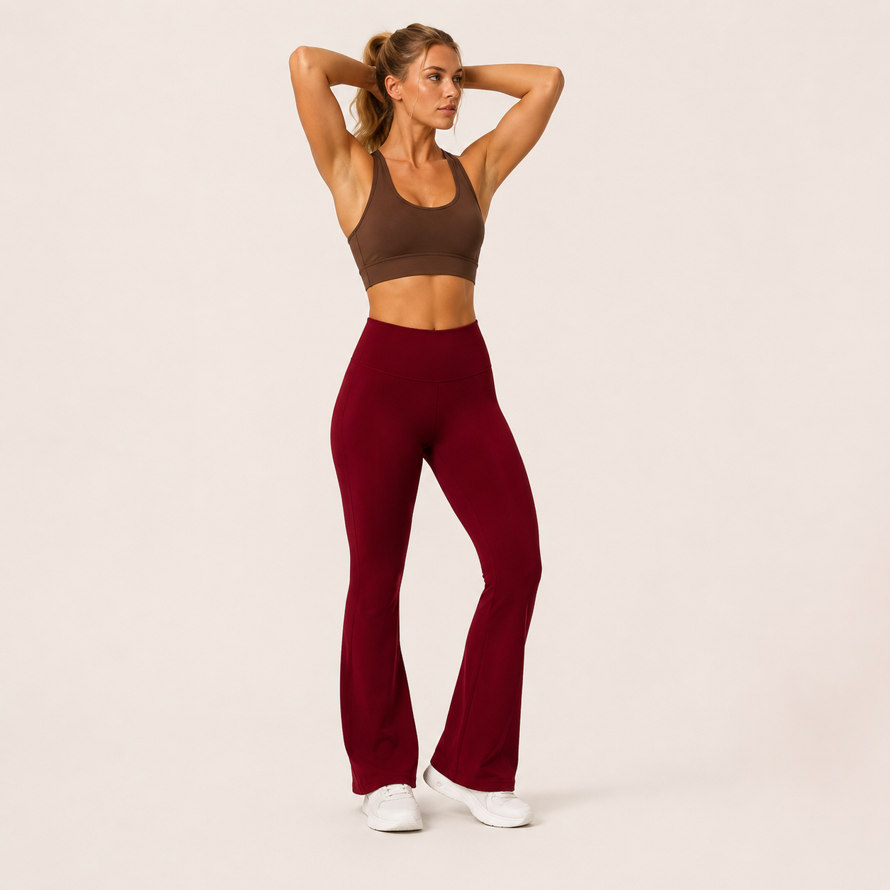 Model wearing the Fitfigura Women’s Booty Boost Yoga Flare Pant in burgundy with a matching sports bra, shown from the front with a high-waist fit and flared legs.