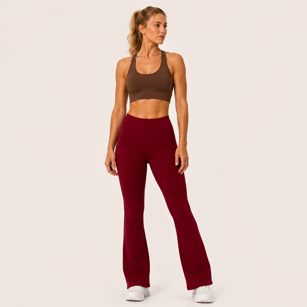 Full-body studio view of the burgundy Fitfigura Women’s Booty Boost Yoga Flare Pant styled with a matching activewear top and white sneakers.