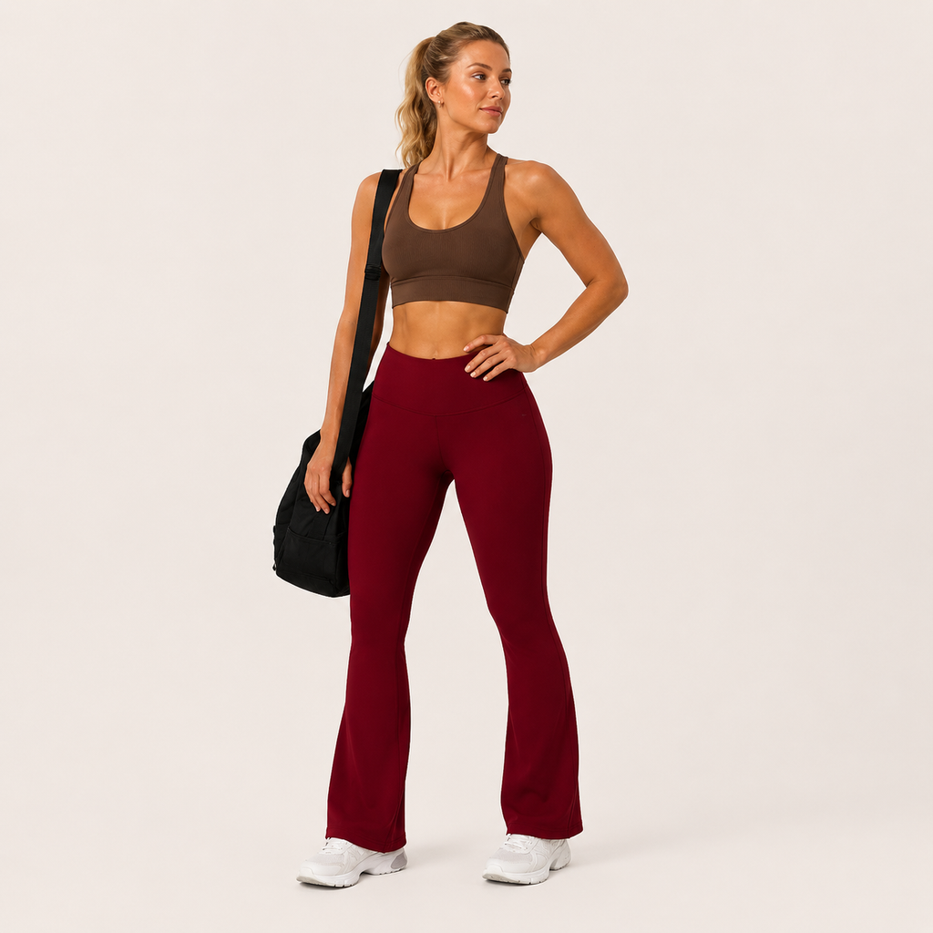 Model wearing the burgundy Fitfigura Women’s Booty Boost Yoga Flare Pant with a matching sports bra and carrying a black bag.