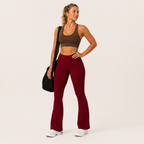 Model wearing the burgundy Fitfigura Women’s Booty Boost Yoga Flare Pant with a matching sports bra and carrying a black bag.