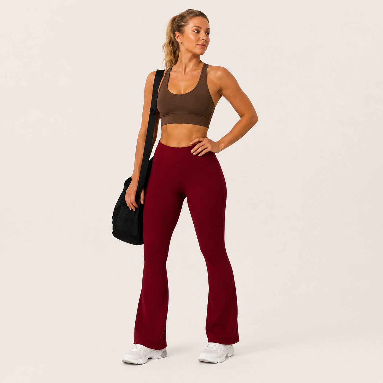 Model wearing the burgundy Fitfigura Women’s Booty Boost Yoga Flare Pant with a matching sports bra and carrying a black bag.