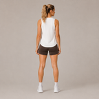Back view of the white Fitfigura Women's in Motion Seamless Tank Top styled with dark shorts and white sneakers.
