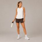 Full-body view of the white Fitfigura Women's in Motion Seamless Tank Top styled with dark shorts, white sneakers, and a black bag.